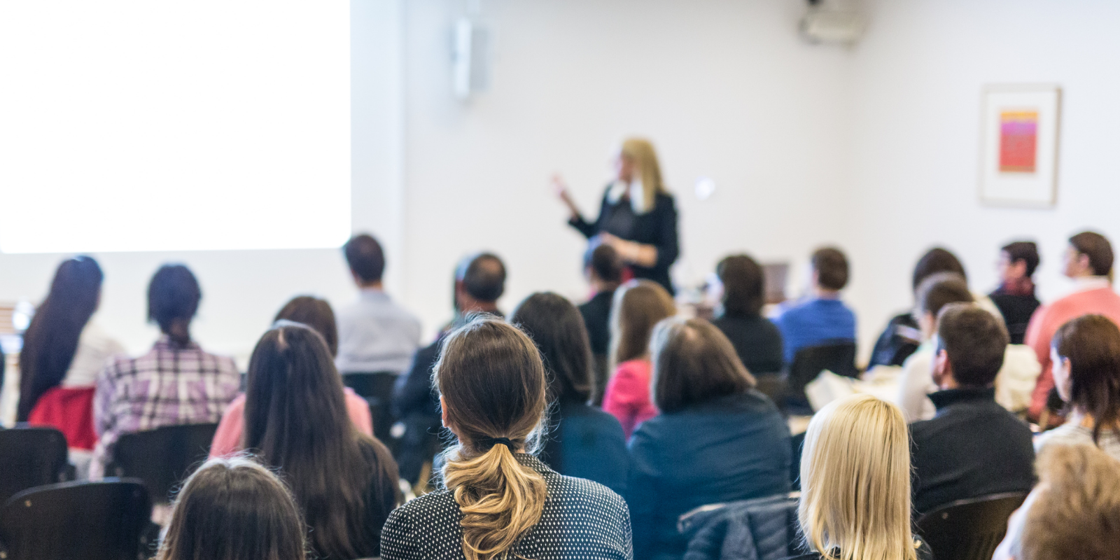 Photo of group watching someone present taken from the back of the room looking towards the front
